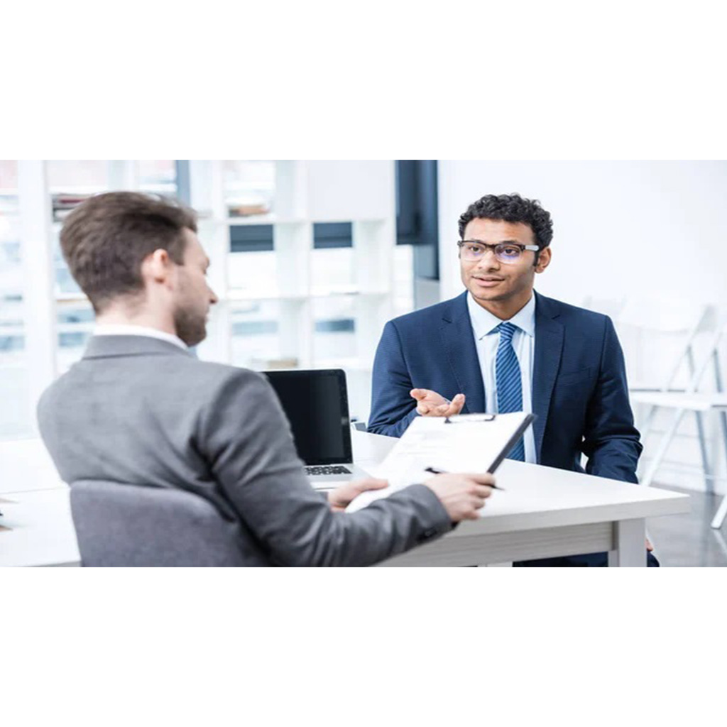 A woman conducting a mock interview with a man, both seated at a table with documents and a water bottle.
